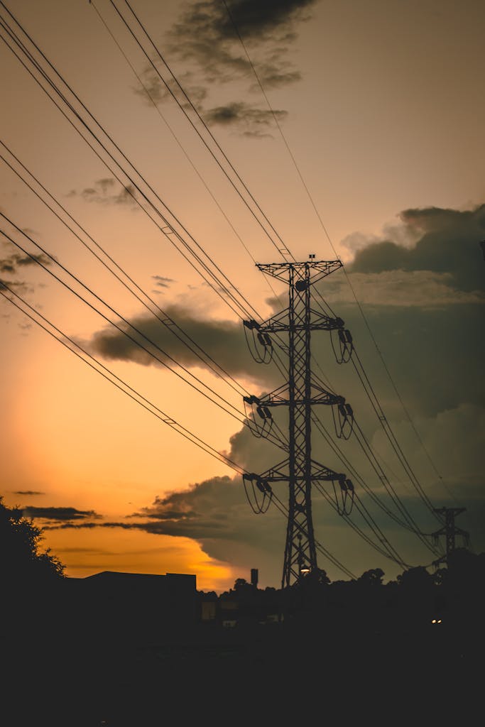 A silhouetted power line tower stretches across a dramatic sunset sky.